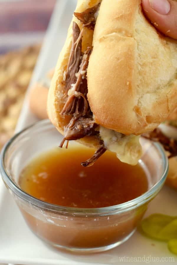 The French Dip Sandwich has shredded beef and melted cheese coming out while being dipped into beef broth. 