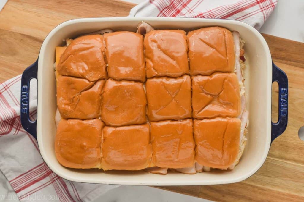 landscape photo of a baking dish on a cutting board with the beginnings of turkey sliders, at the step of adding the tops of the slider rolls