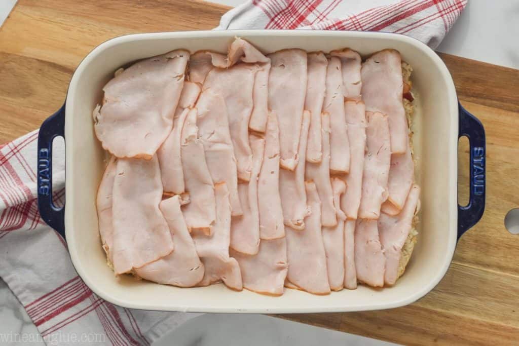 landscape photo of a baking dish on a cutting board with the beginnings of turkey sliders, at the step of adding folded deli turkey