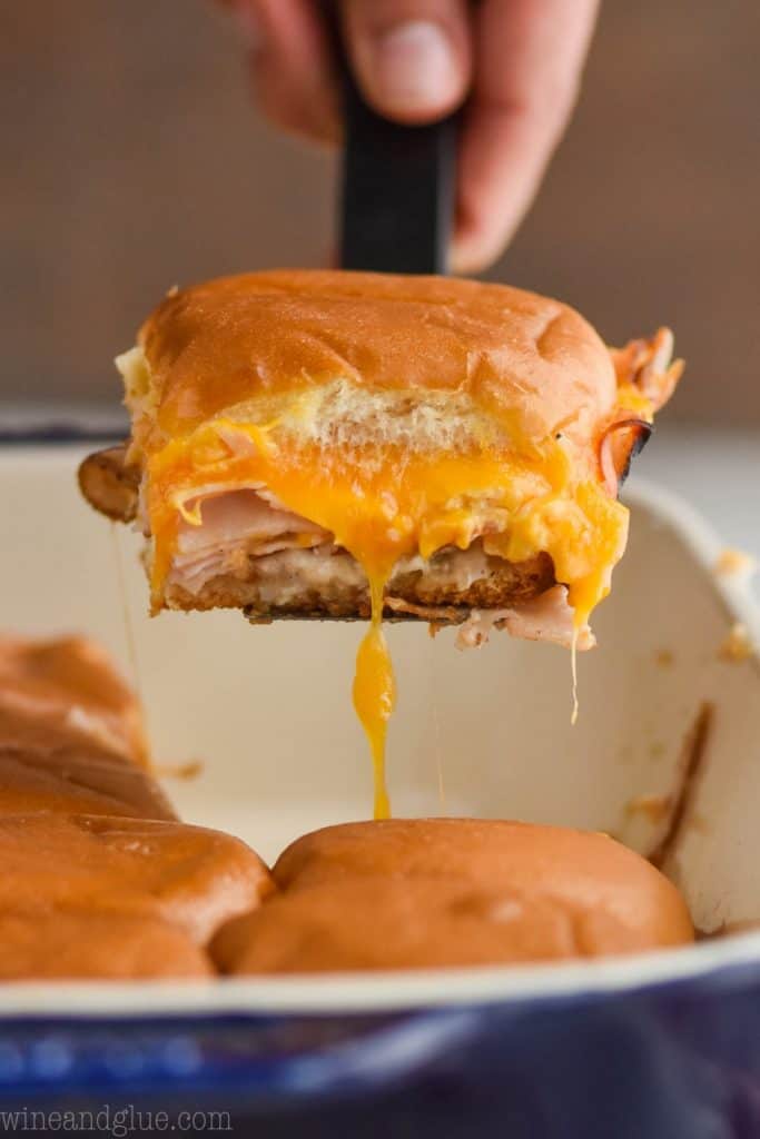 a turkey slider coming out of the pan with cheddar cheese stretching down