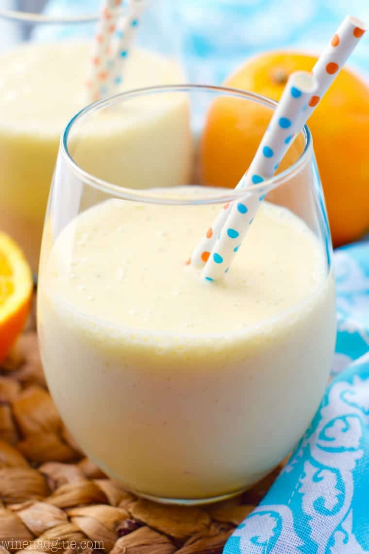 In a glass, the Orange Colada Smoothie has a pastel yellow color and two paper straws with polka dots. 