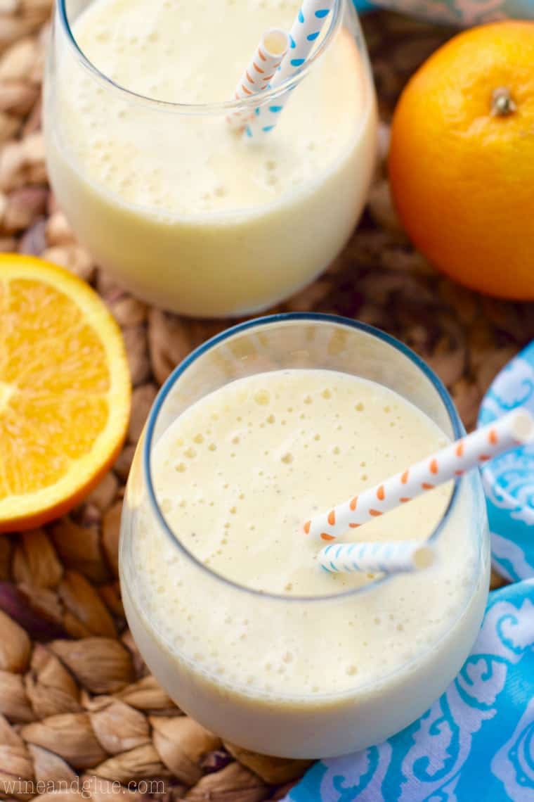 An overhead photo of two Orange Colada Smoothie that has a pastel yellow color and sliced oranges around the glasses. 