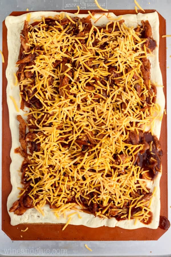 A layer of pizza dough with the BBQ shredded chicken topped with shredded cheddar cheese. 