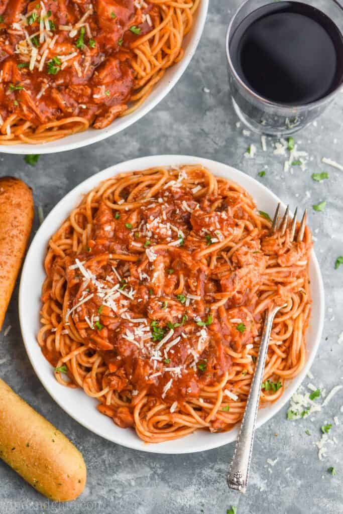 overhead view of a small white plate that has spaghetti with a red sauce made with shredded chicken and a fork twisted in it