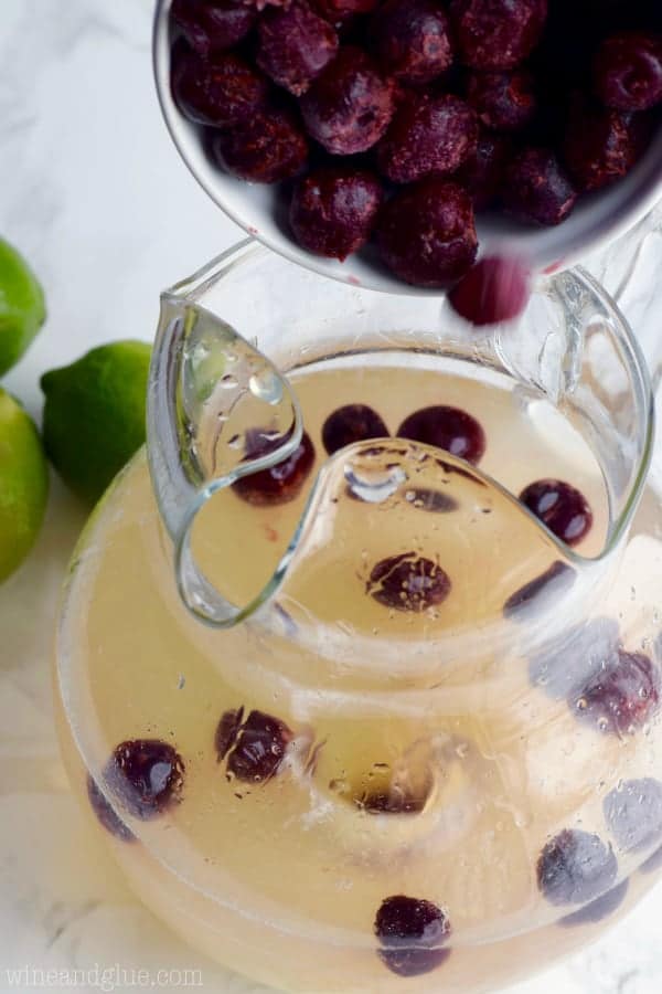 A bag of frozen cherries is being poured into the pitcher with the frozen limeade, cherry vodka, and white wine