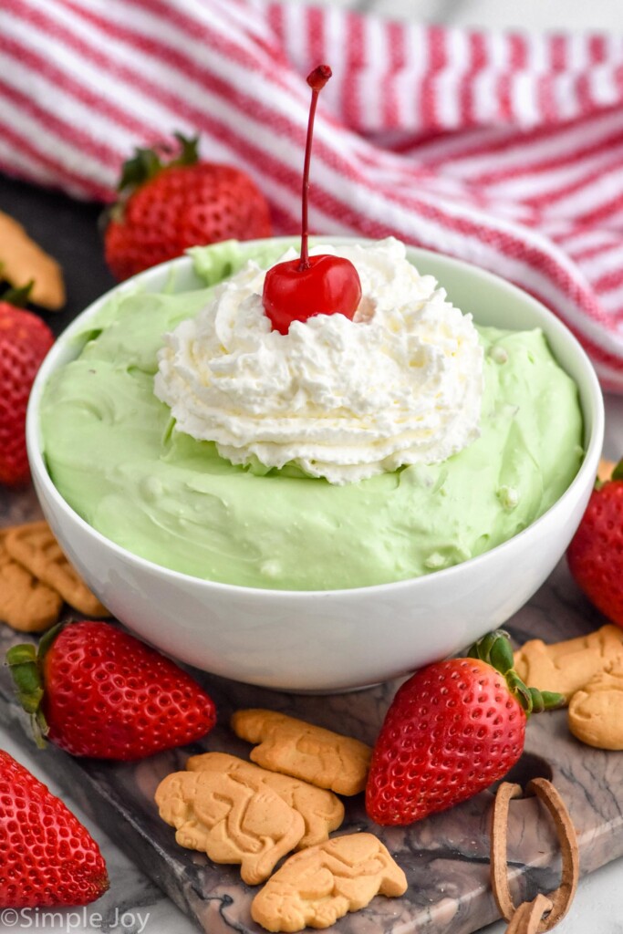 a white bowl full of pistachio dip with strawberries and crackers around it