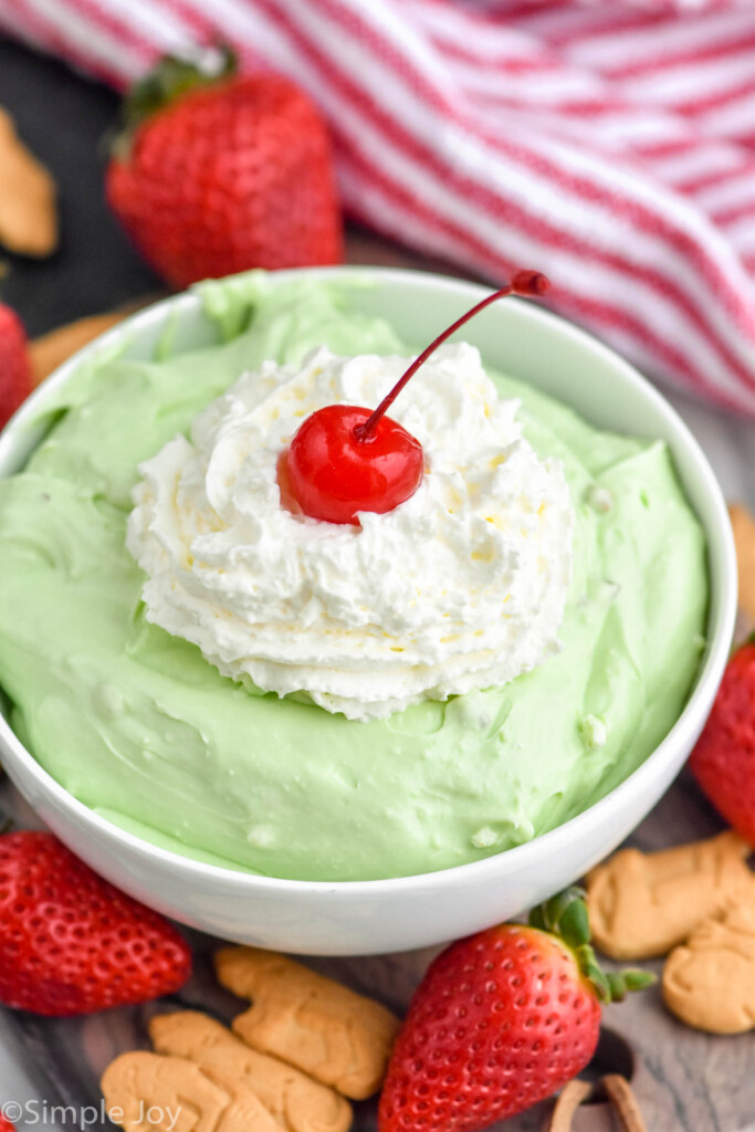 bowl of green pistachio cheesecake dip topped with whipped cream and a cherry
