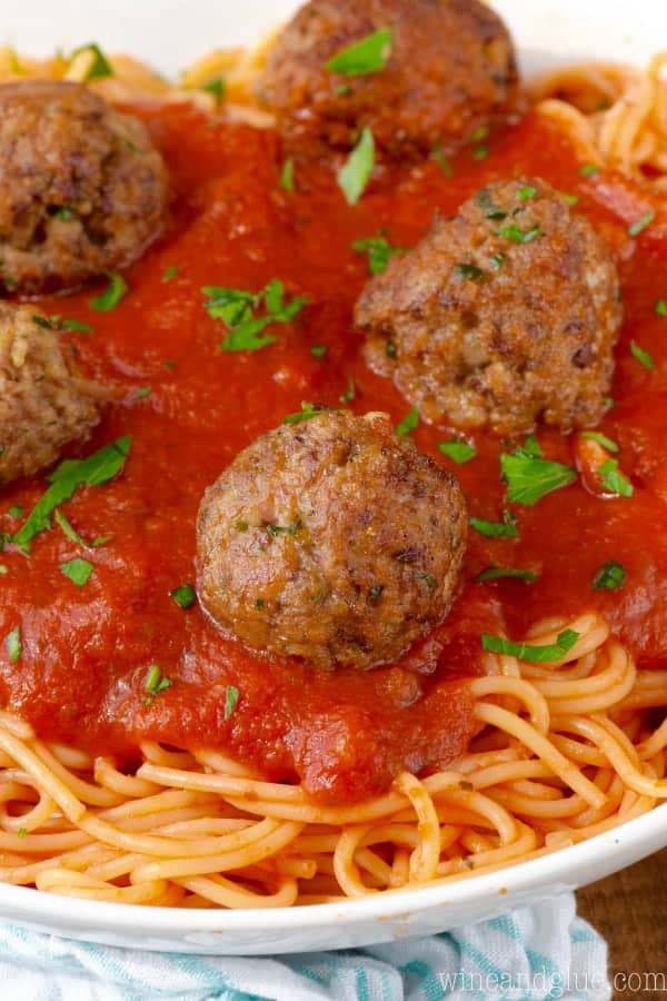 a close up of 6 meatballs on red sauce on spaghetti with fresh parsley as a garnish