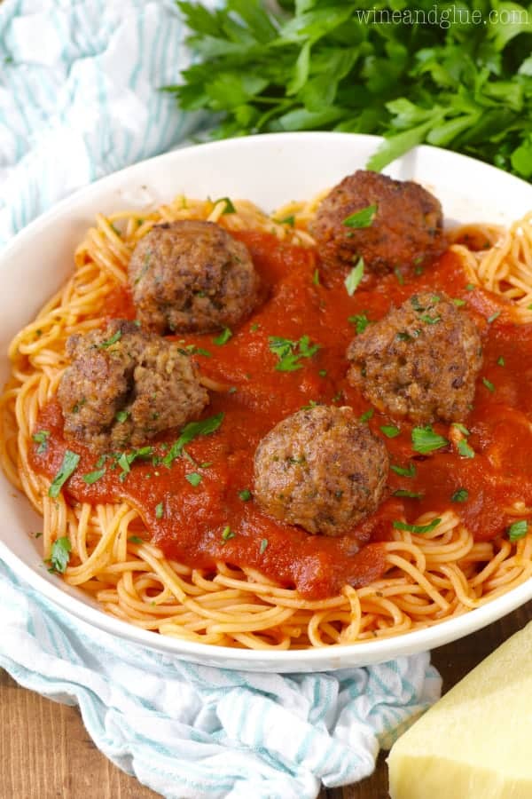 a white bowl filled with spaghetti and topped with red sauce and five Italian meatballs