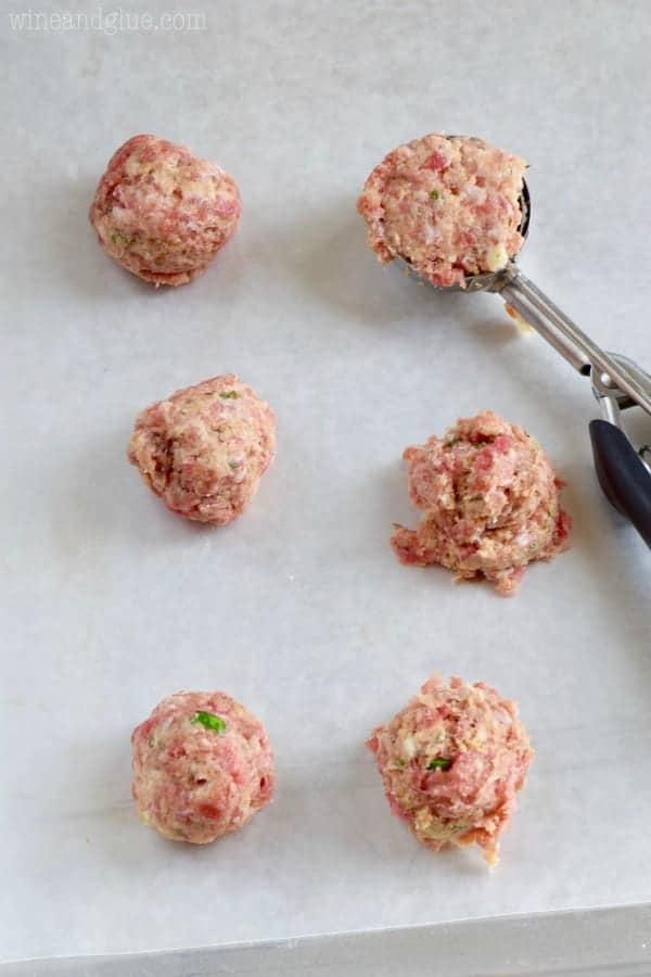 close up of a parchment lined baking sheet where a cookie scooper has formed six Italian meatballs before baking