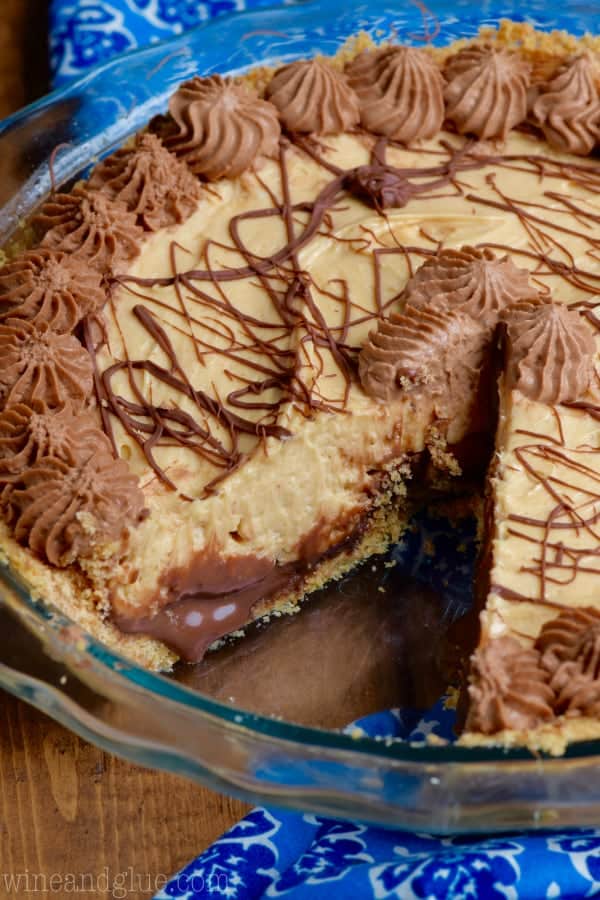 a whole peanut butter cup pie with a piece cut out of it, chocolate drizzled on top, and chocolate whipped cream piped around the edges