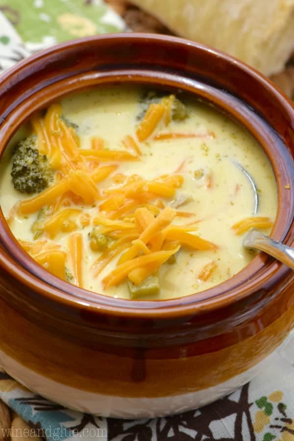 a close up of a brown bowl of broccoli cheddar soup topped with cheddar cheese