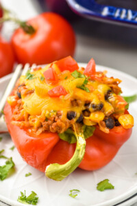 a taco stuffed pepper on a plate topped with chopped tomatoes and cilantro