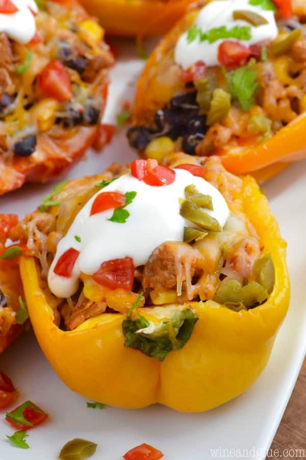 close up of a taco stuffed bell pepper topped with sour cream, cilantro, pickled jalapeño pieces and chopped tomatoes