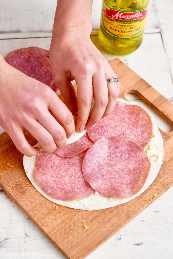tortilla with salami on it being rolled up