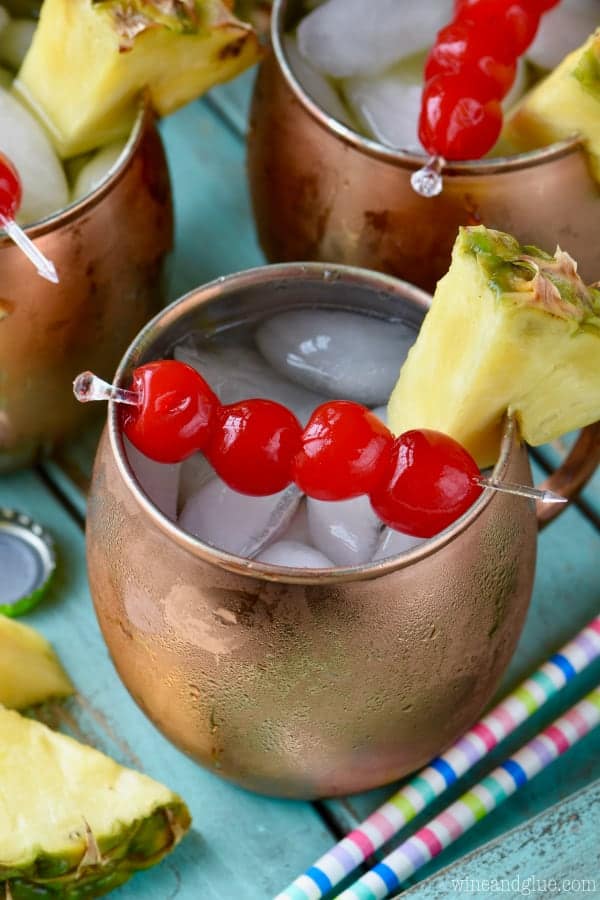 In copper mugs, the Tropical Moscow Mules have ice cubes and on the rim there are sliced pineapples and cherries. 