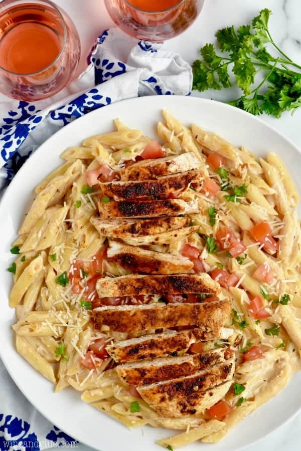 overhead view of a plate of spicy and creamy chicken pasta on a plate with two glasses of rose