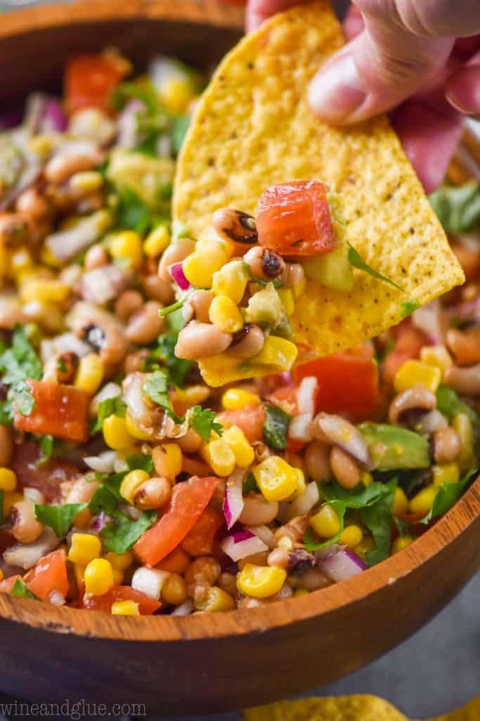 close up of a tortilla chip dishing up texas caviar recipe with black-eyed peas, tomatoes, and corn 
