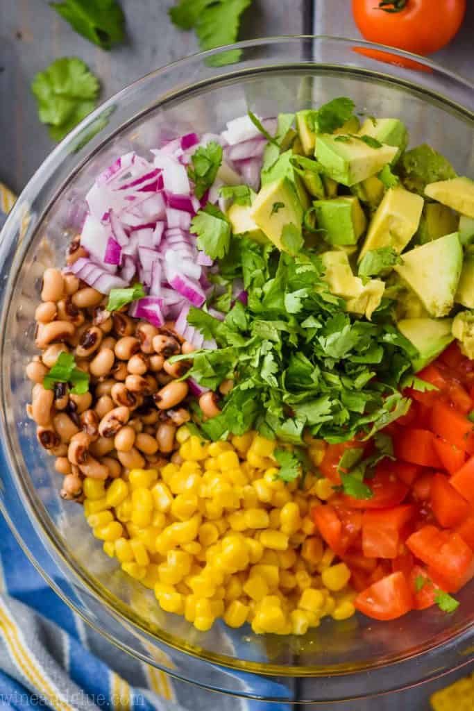 overhead view of cowboy caviar recipe broken down by ingredient - red onions, avocado pieces, tomatoes, corn, black eyed peas and cilantro in the middle