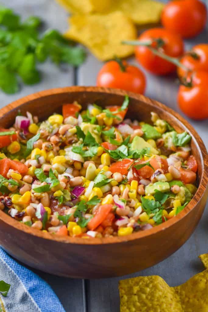 texas caviar in a wood bowl full of black eyed peas, cilantro, chopped up tomatoes, corn, and red onion