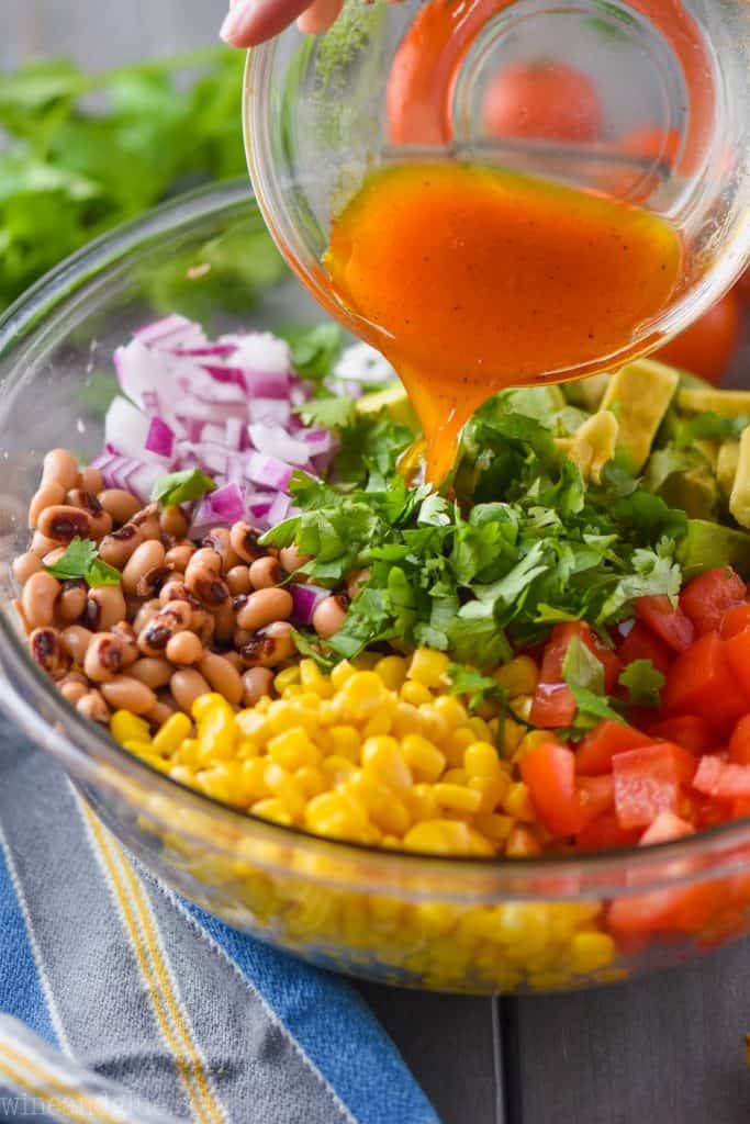 side view of a vinaigrette dressing being poured over a bowl full of ingredients to make cowboy caviar