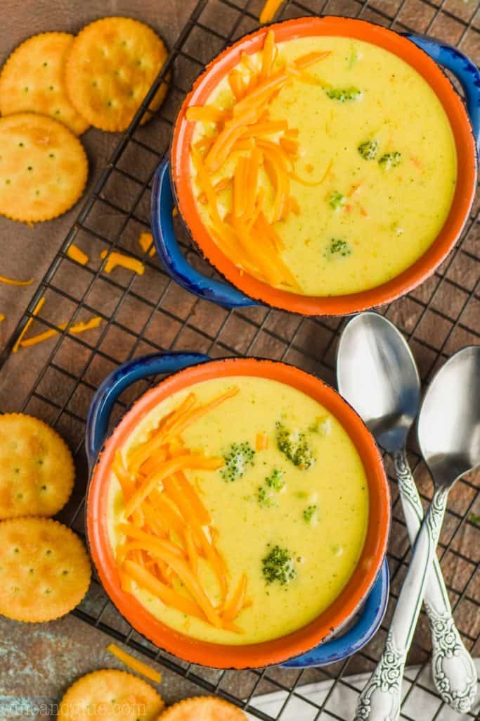 An overhead photo of two bowls of Broccoli Cheddar Soup with cheddar cheese sprinkled on one side and Ritz Crackers next to the bowl 