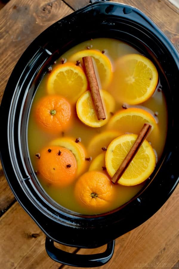 overhead view of a crockpot to make spiced apple cider filled with orange slices studded with cloves and cinnamon sticks