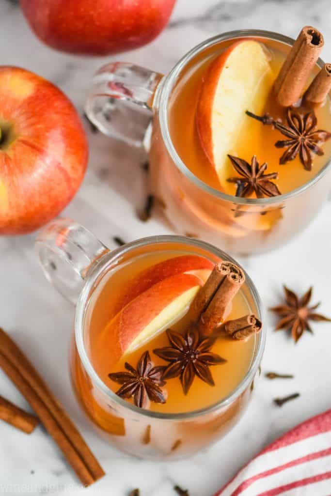 overhead view of two clear mugs full of crockpot spiced apple cider and garnished with star anise, sliced apples and cinnamon sticks