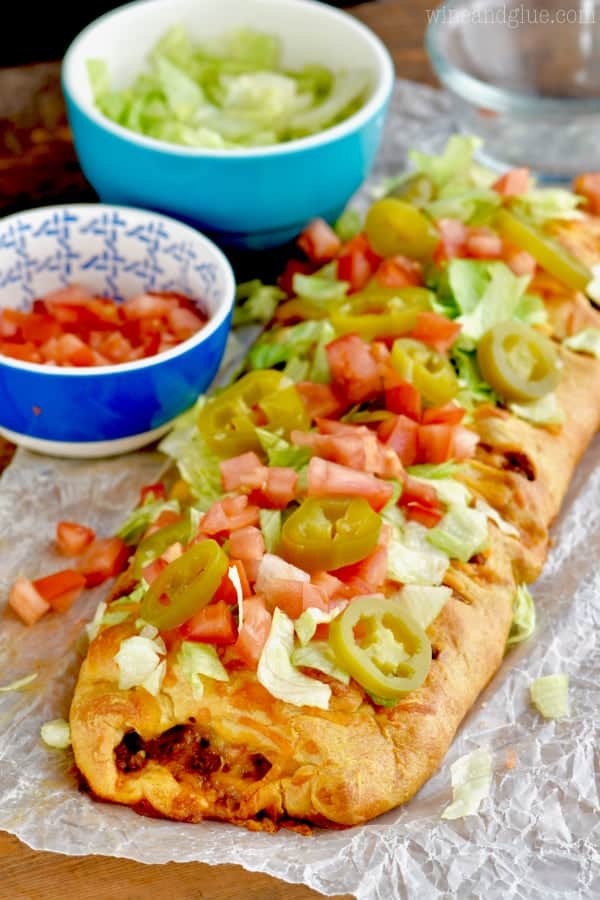 On a tin foil, the taco braid is topped with diced tomatoes, lettuce, and pickled jalapenos. 