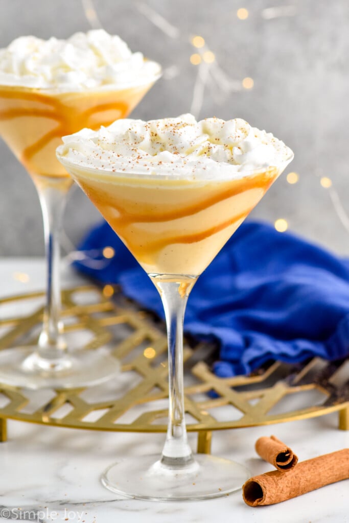 two martini glasses lined with caramel sauce with an eggnog martini, topped with whipped cream