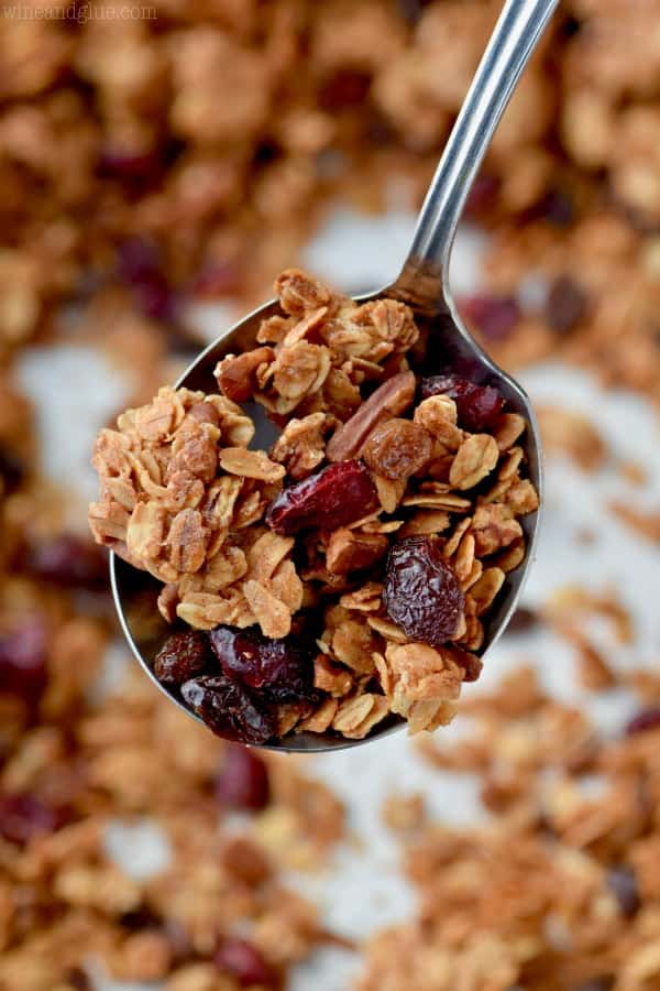 metal spoon holding a spoonful of granola recipe with oats, nuts and dried cranberries visible