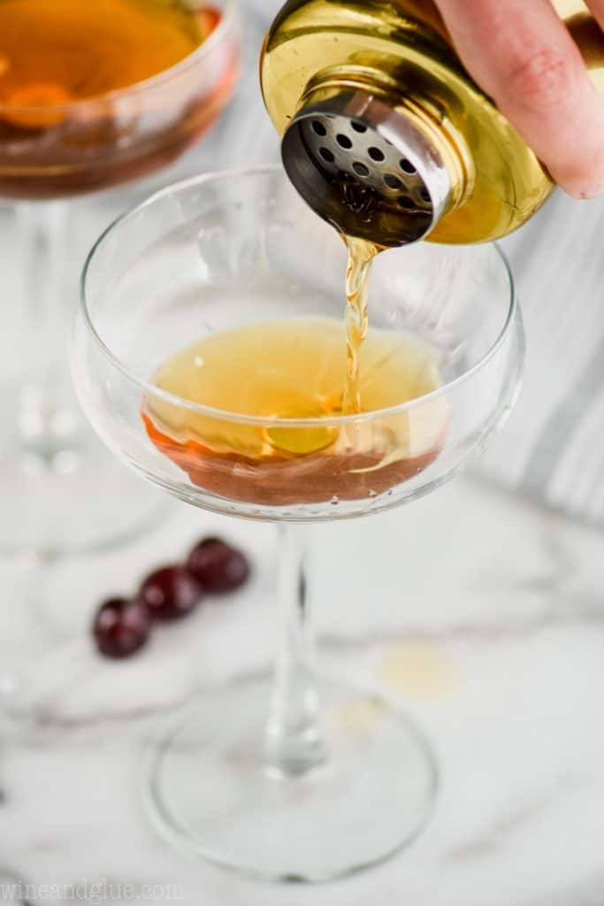 a Manhattan cocktail being strained into a champagne coupe glass