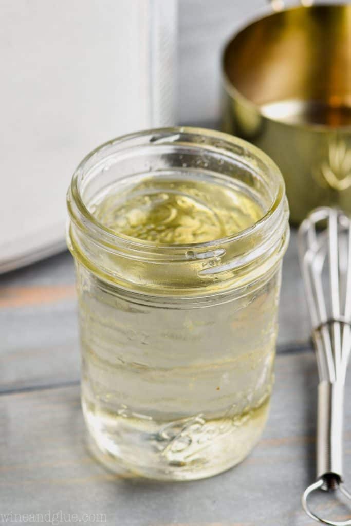 simple syrup in a mason jar with a metal whisk next to it and a gold measuring cup in the background to show how to make simple syrup