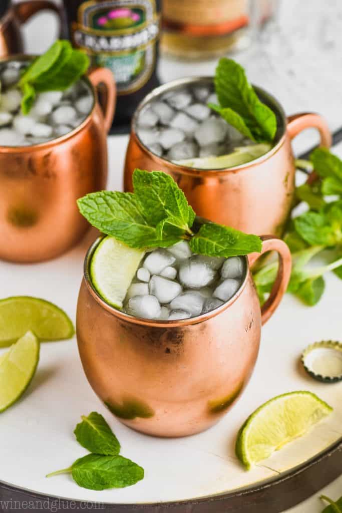 a moscow mule recipe in three copper mugs filled with ice and garnished with mint and lime