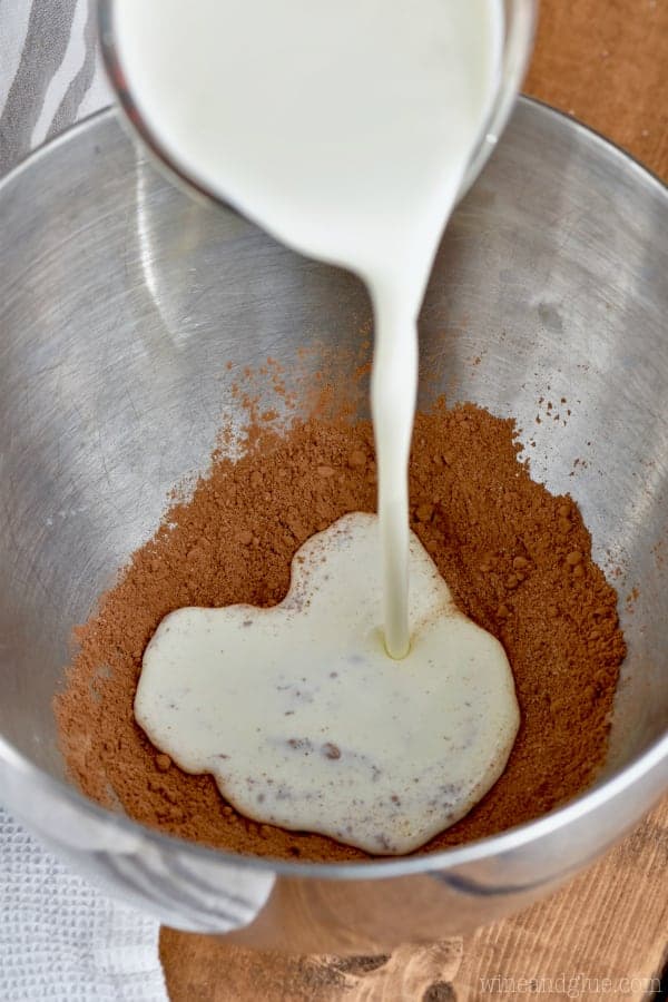 heavy cream being poured onto a mixture of cocoa powder and sugar in a metal bowl to make chocolate whipped cream