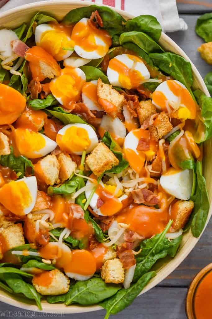 spinach salad with croutons and eggs in a white salad bowl topped with red spinach salad dressing