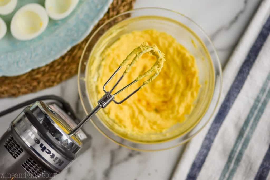 overhead view of a hand mixer that has just mixed a small bowl of the yellow yolk mixture for deviled eggs