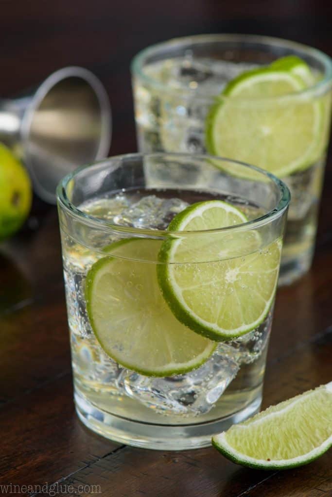two glasses of gin and tonic, each garnished with lime slices and full of ice