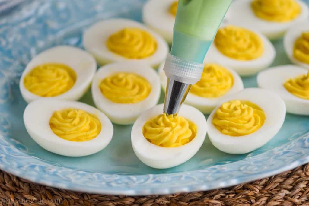 side view of piping the center into a deviled egg using a blue piping bag