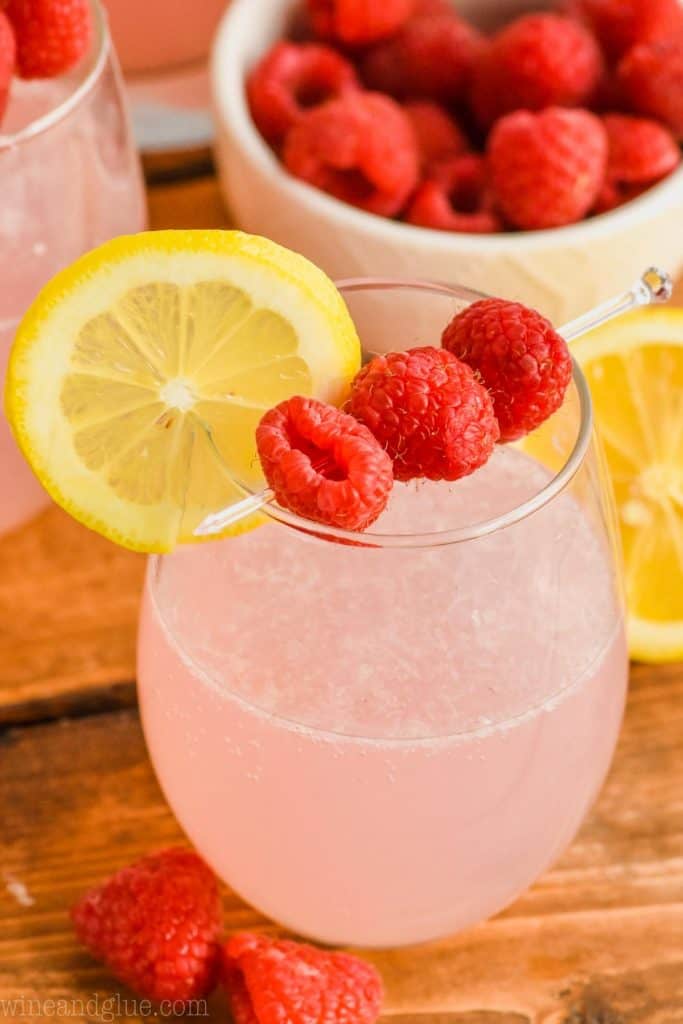 stemless wine glass full of pink lemonade vodka punch garnished with a lemon slice and some fresh raspberries