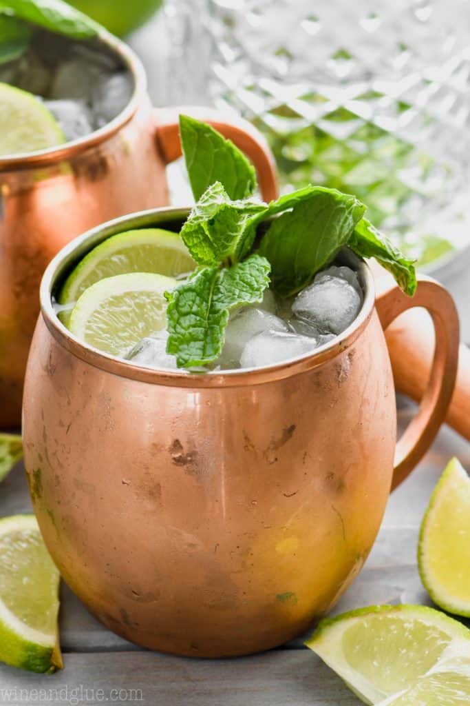moscow mule with gin in copper mug garnished with mint and lime, a mixing glass in the background
