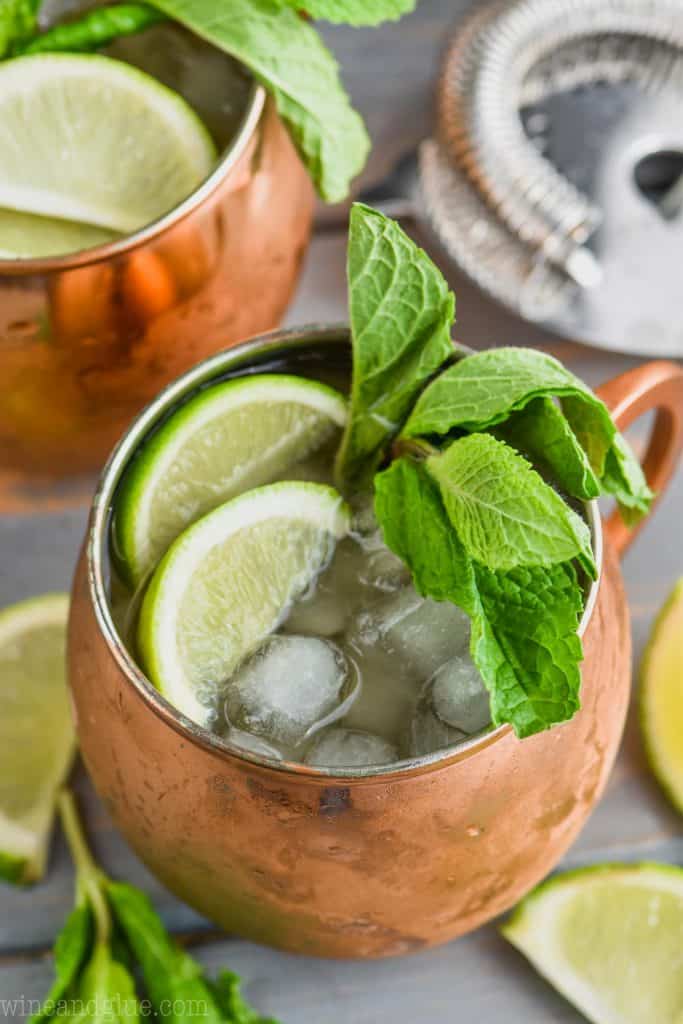 gin gin mule from above in copper mug garnished with lime and mint, cocktail strainer in the background and other copper mug