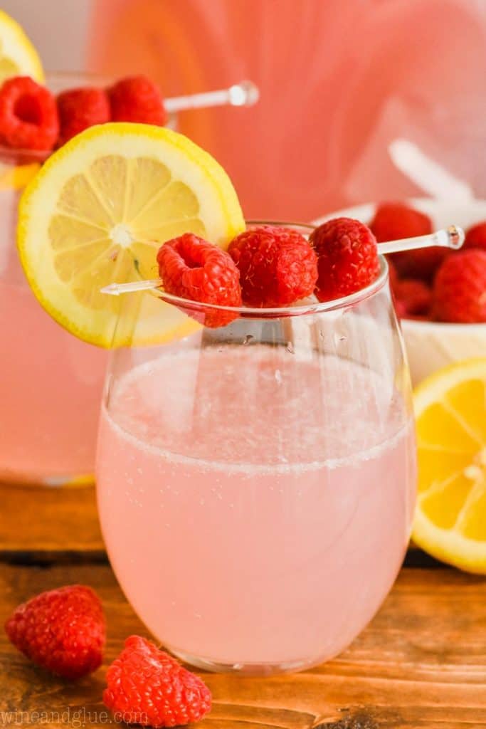 stemlesss wine glass with a lemon slice and three raspberries skewered over a pink lemonade vodka punch