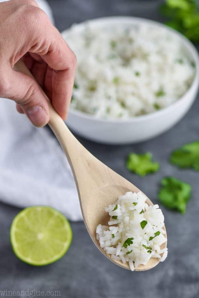 spoonful of rice with lime and cilantro with bowl in the background