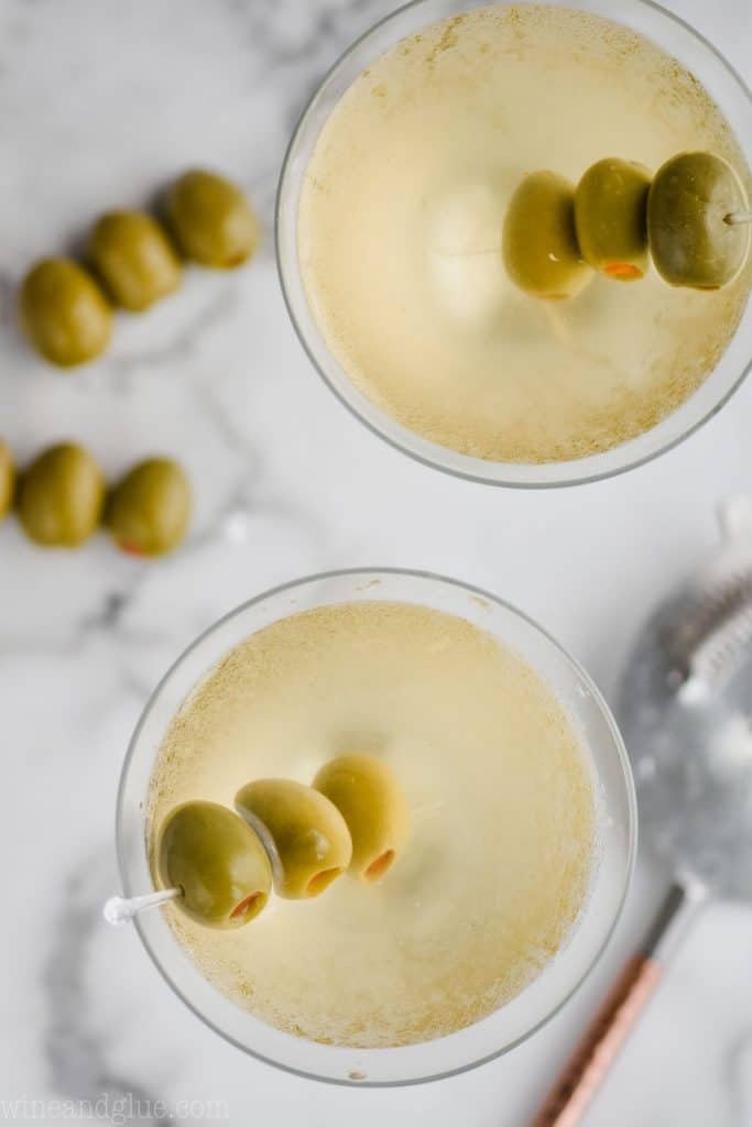 overhead view of two martini glasses filled with vodka martini dirty with three olives in each glass