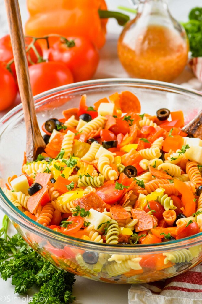 wooden serving spoons sticking out of a large glass bowl with Italian pasta salad, garnished with parsley
