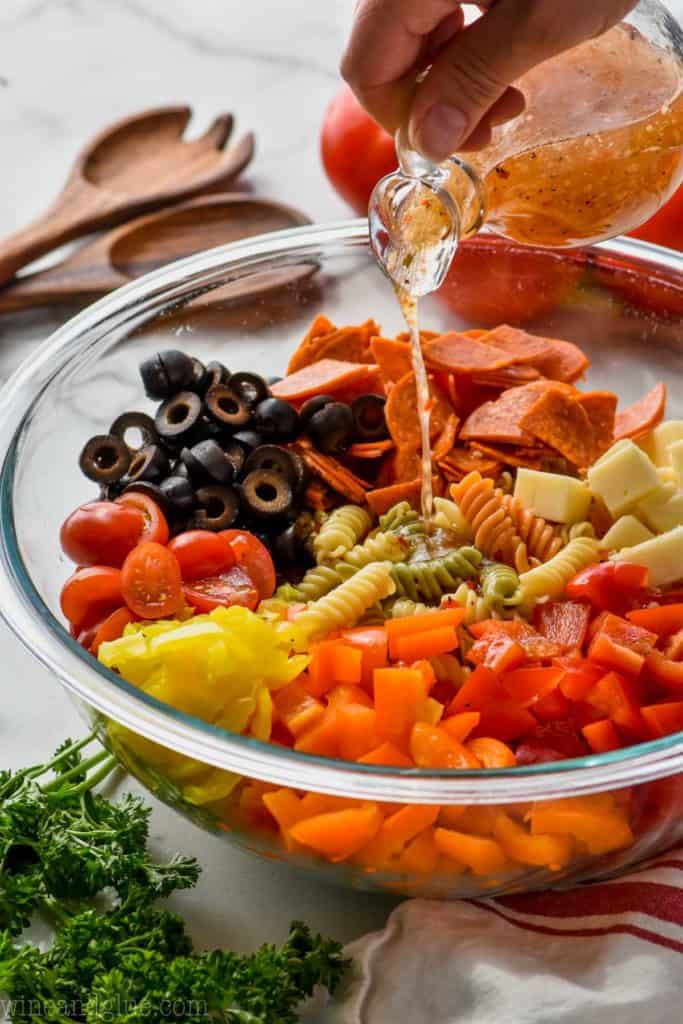 pouring Italian dressing on pasta salad