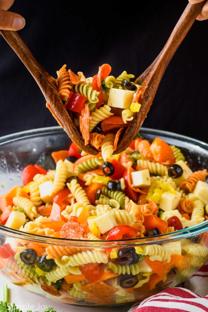 wooden spoons scooping up italian pasta salad from a large clear bowl