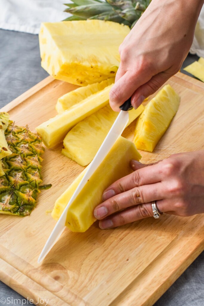 a pineapple being cut into spears on a cutting board