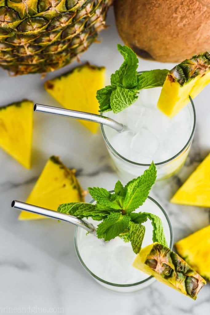 overhead view of two pineapple mojitos garnished with fresh mint, pineapple wedges, and pineapple wedges laying next to it